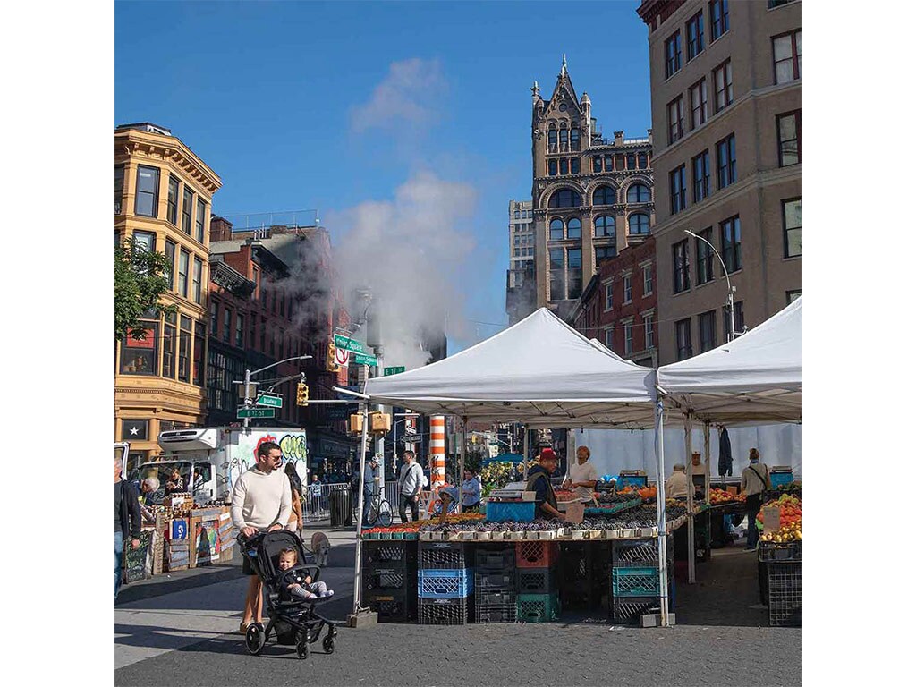 Street fair tents in city intersection with person pushing baby stroller in foreground