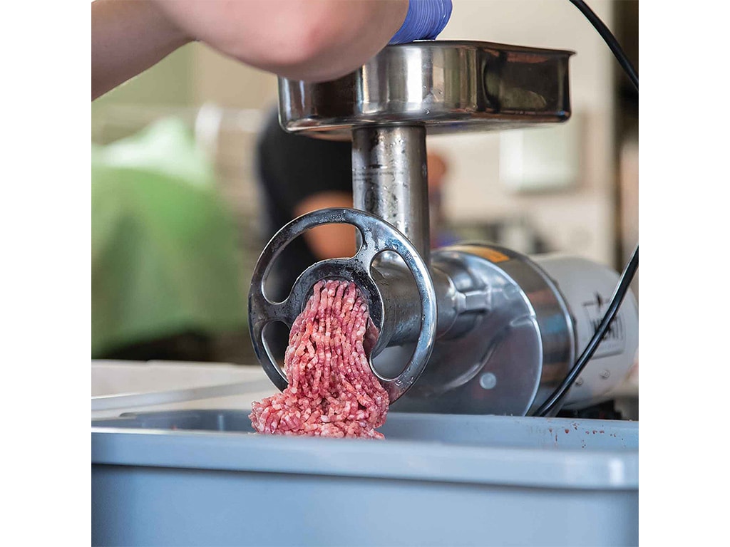 a meat grinder with ground pork coming out of it into a plastic bin