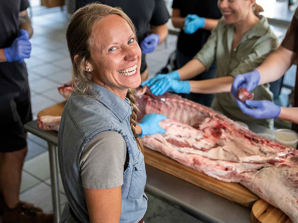a smiling person with people participating in the butchering process around a table