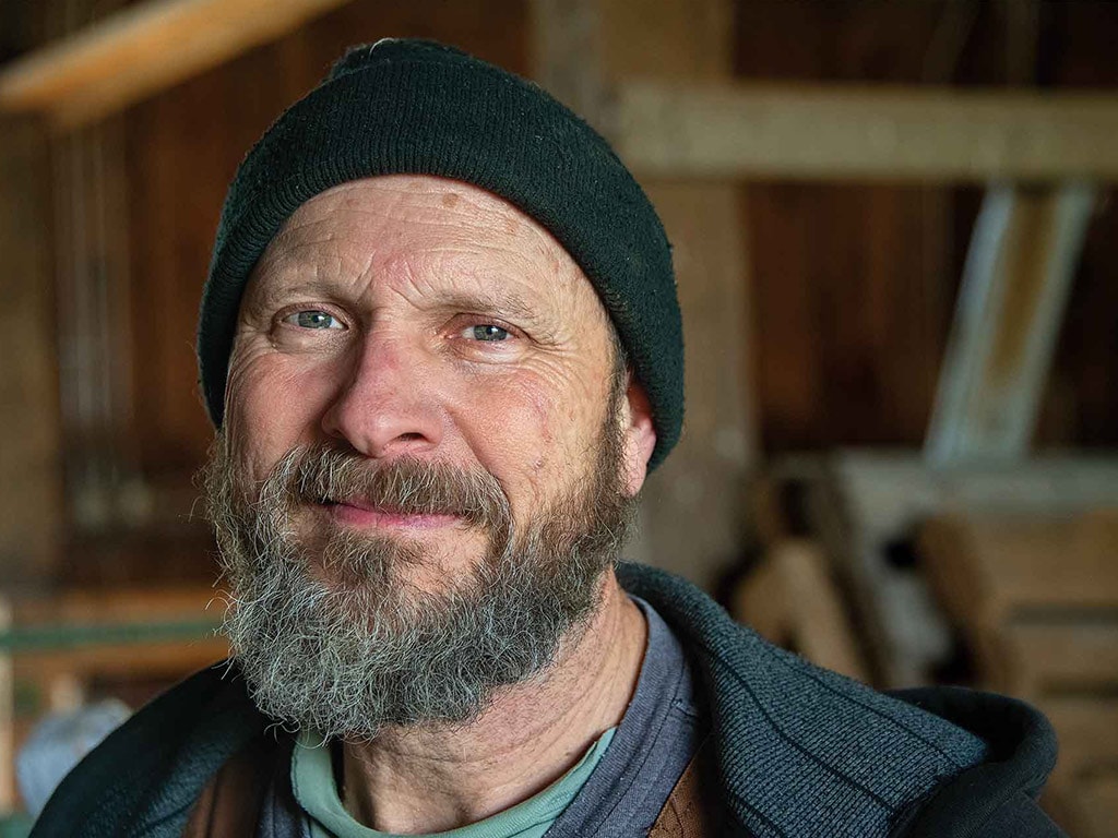 a smiling person with a greyish beard and black ski cap on