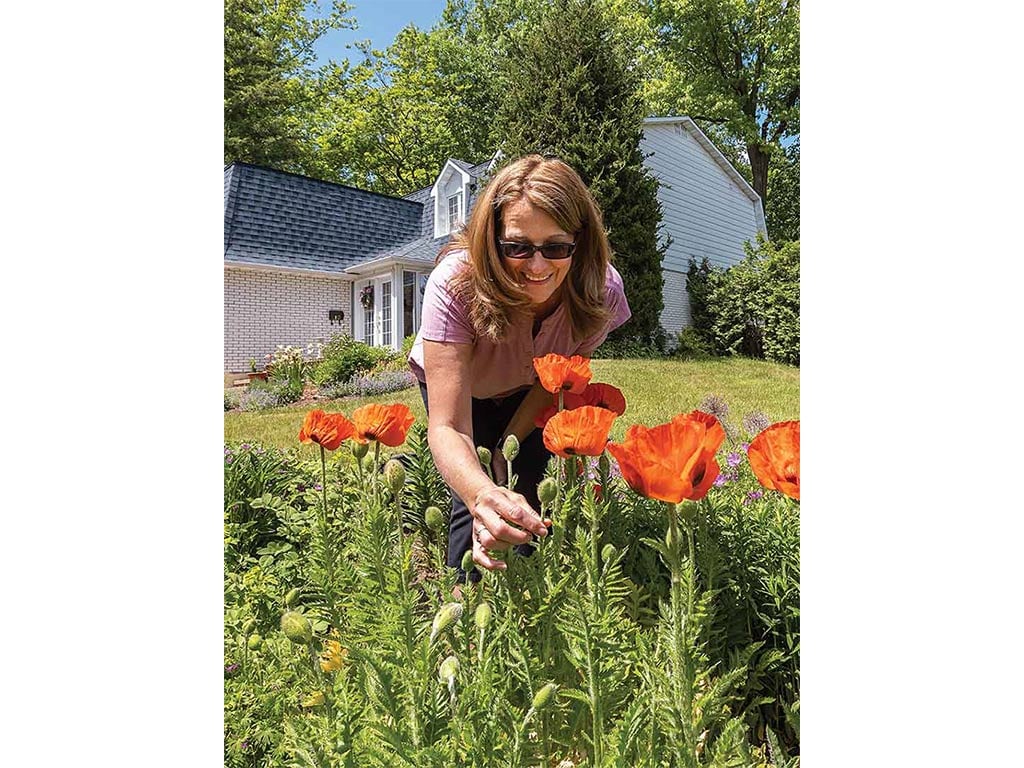 a person bending over holding a flower stem in a home garden