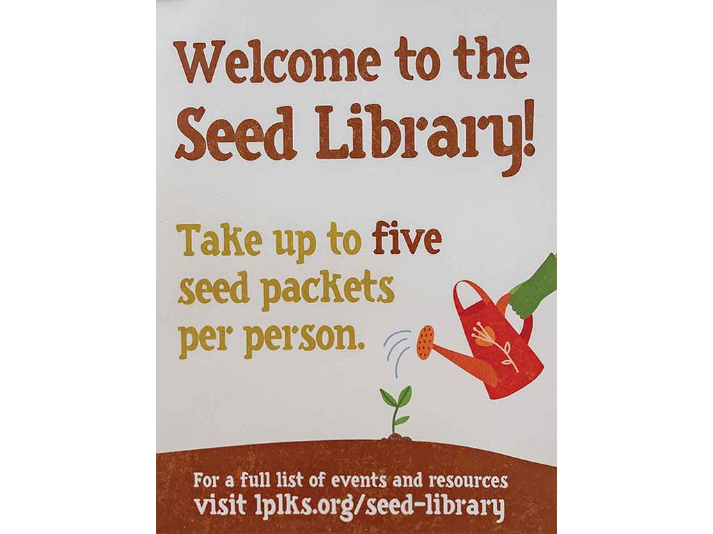 a seed library sign with a website link and a painting of a garden-gloved hand with a watering can