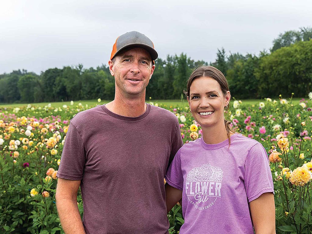 two smiling people standing in a field of flowers