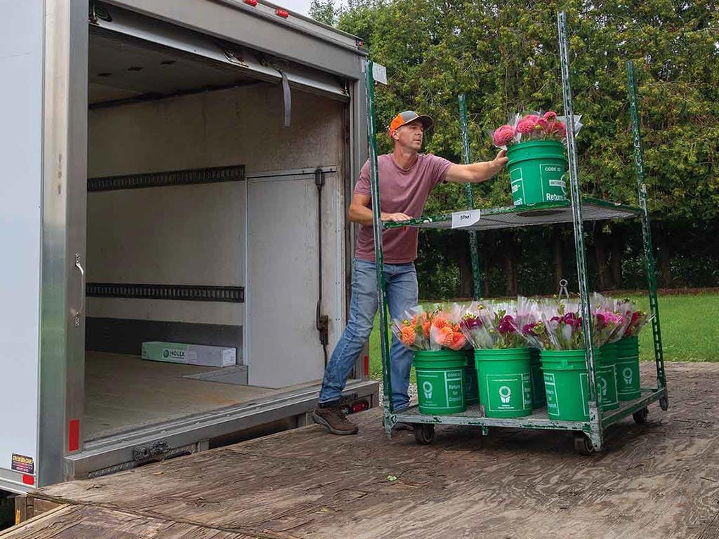 a person loading green buckets of flowers onto a box truck from a rolling cart