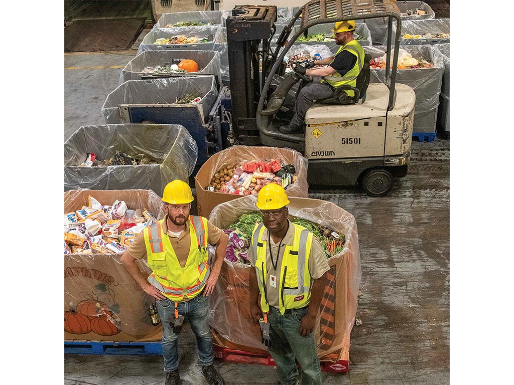 Two people with yellow hard hats and safety vests looking up from warehouse floor