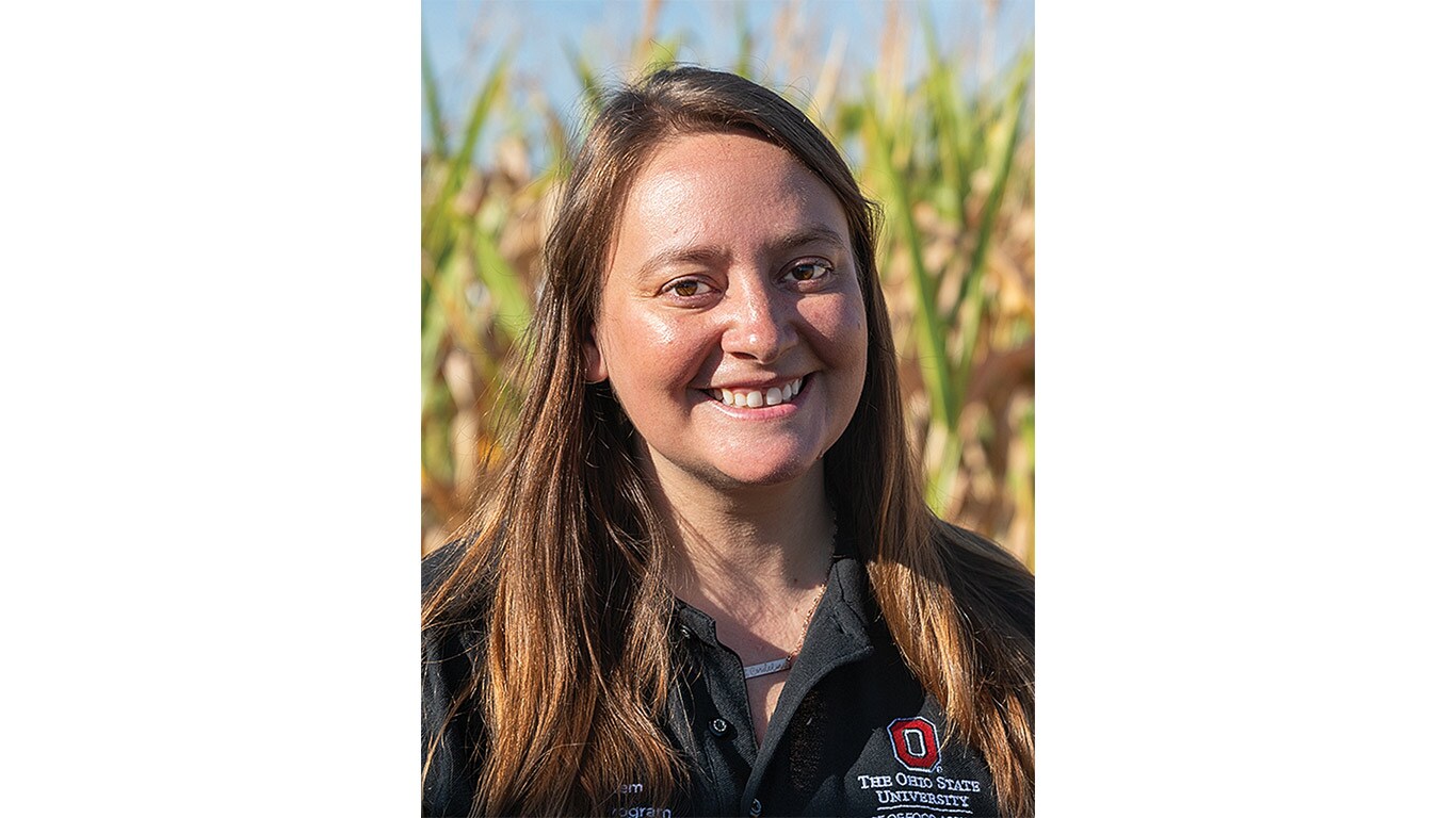 A person wearing a dark shirt with the Ohio State University logo stands in front of a cornfield.