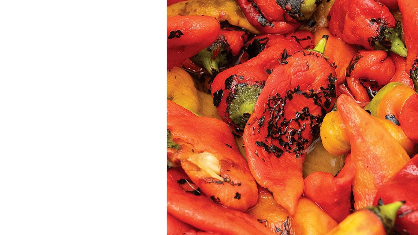 Roasted red, orange and yellow peppers with black char marks in a close-up pile.