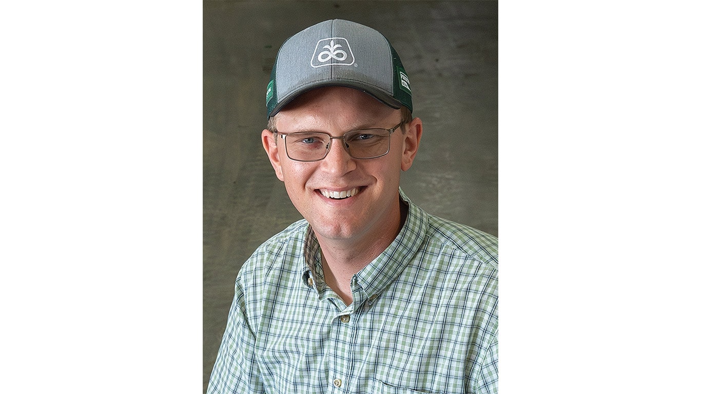 Person in checkered shirt and cap sitting indoors, smiling