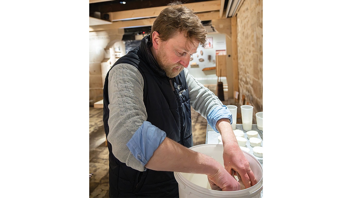 Une cuve de fromagerie en cuivre avec un outil de coupe devant une exposition muséale sur l'histoire de la fabrication du fromage.
