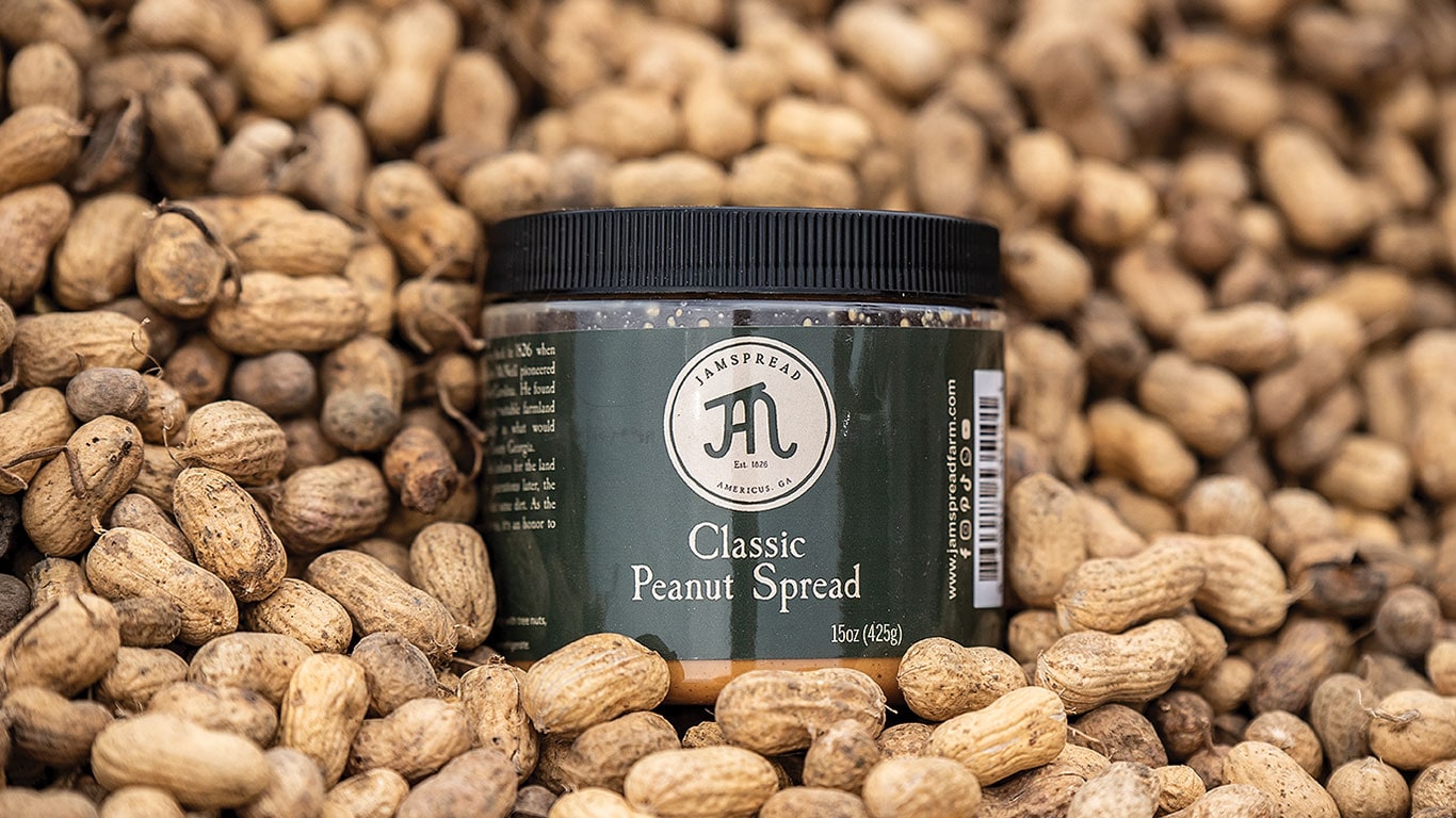 Jar of classic peanut spread placed on a pile of unshelled peanuts in close-up view.