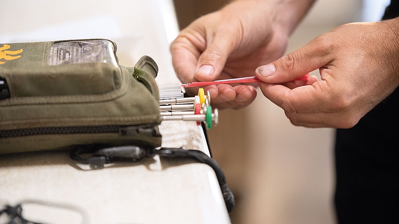 Les mains d'une personne tiennent un outil rouge tout en organisant des tournevis codés par couleur dans une pochette verte.