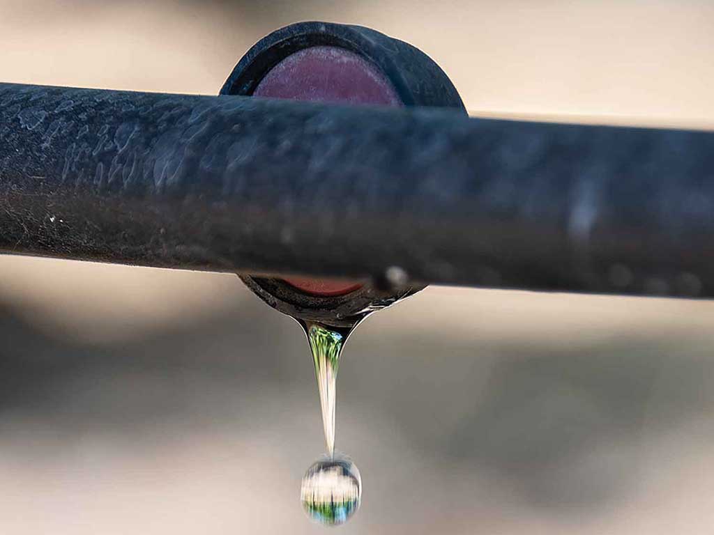 A closeup of water droplet dropping underneath water conservation pipe