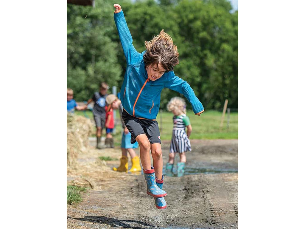 A child jumping mid-air with one arm upwards on dirt trail