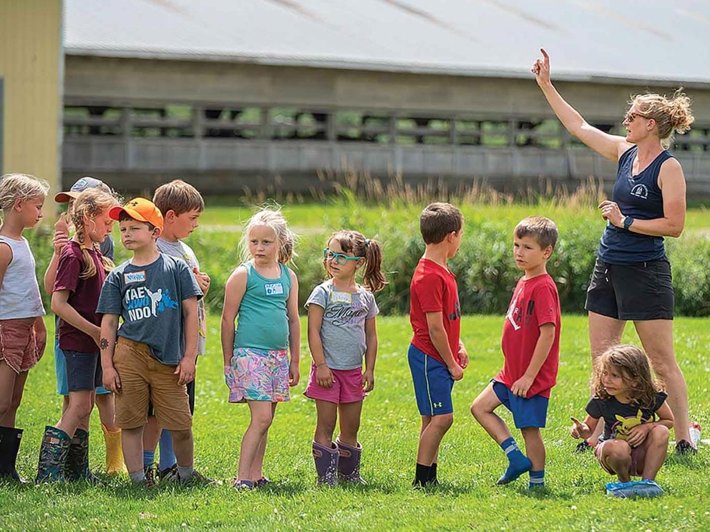 Children lined up in grass field with an adult leading them
