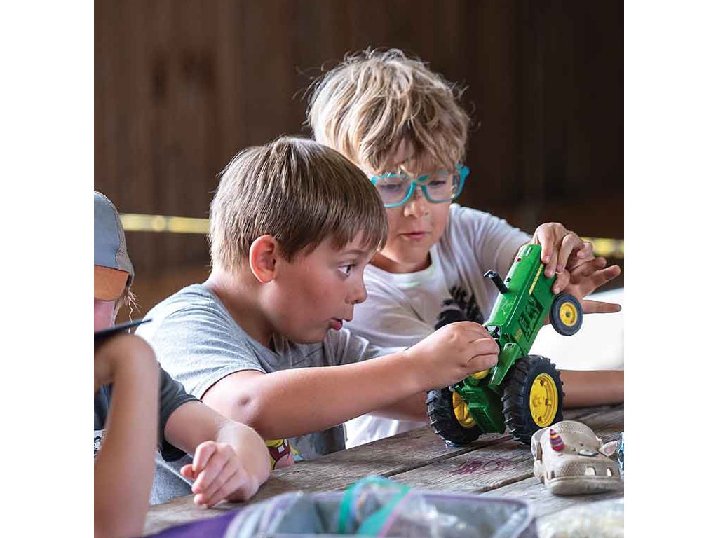 Two children playing with John Deere toy tractor on table