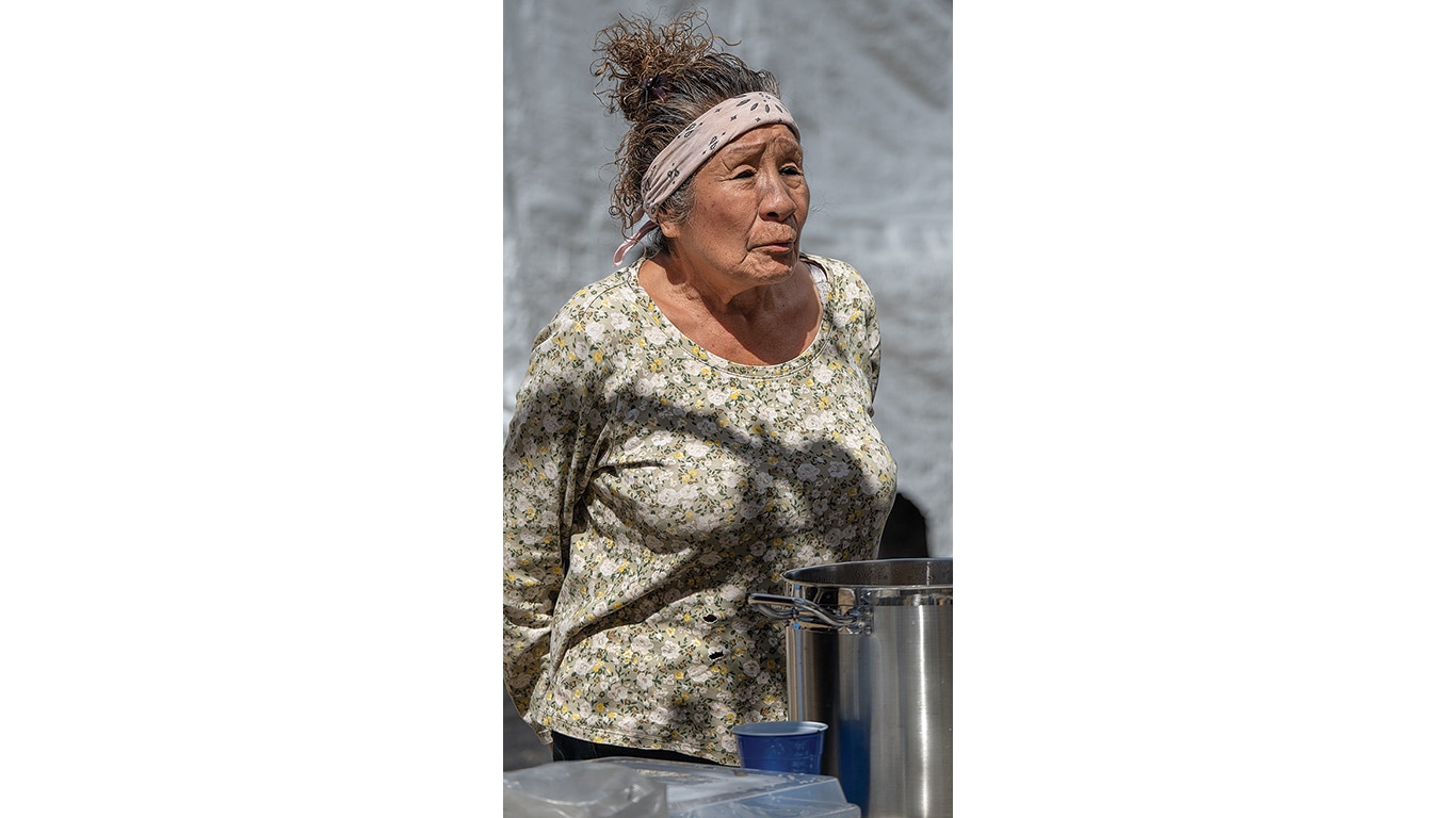 Woman stands beside a large pot during outdoor cooking.