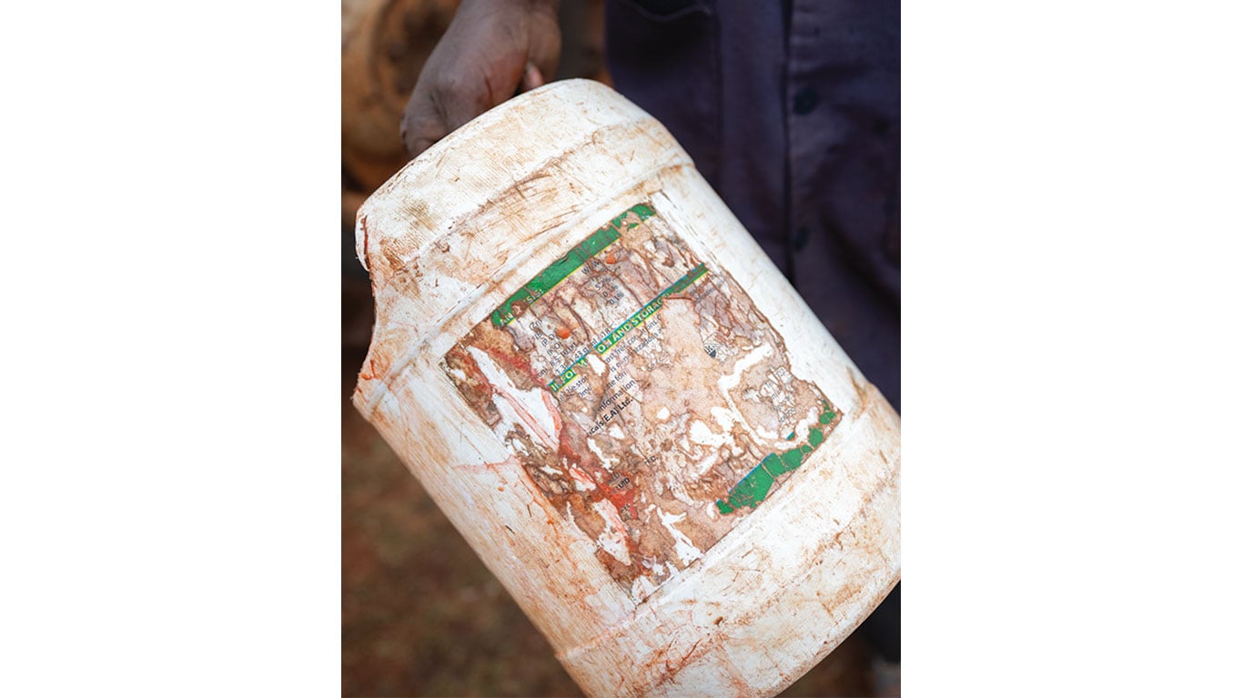 Empty, dirt-stained pesticide container held in a person&rsquo;s hand, showing a worn and partially removed label.