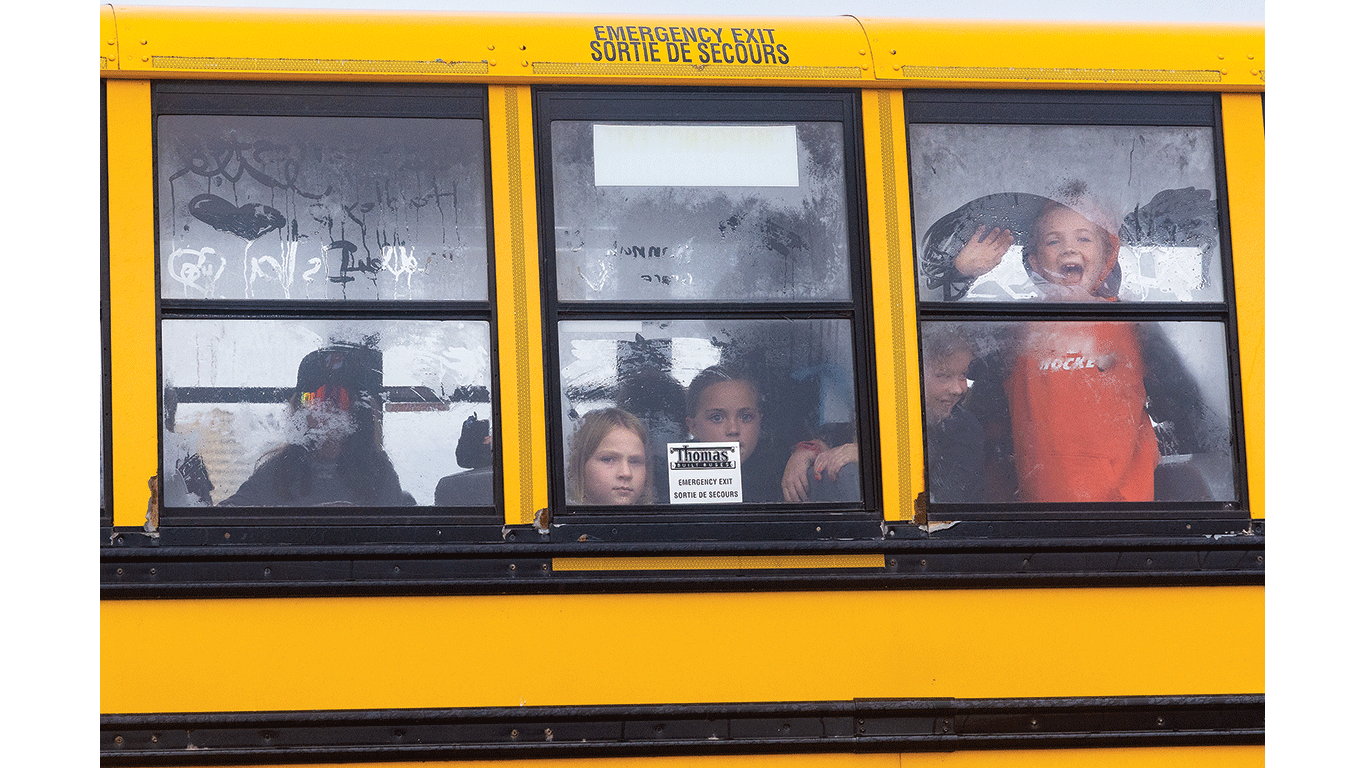 Several children look out fogged windows of a yellow school bus.