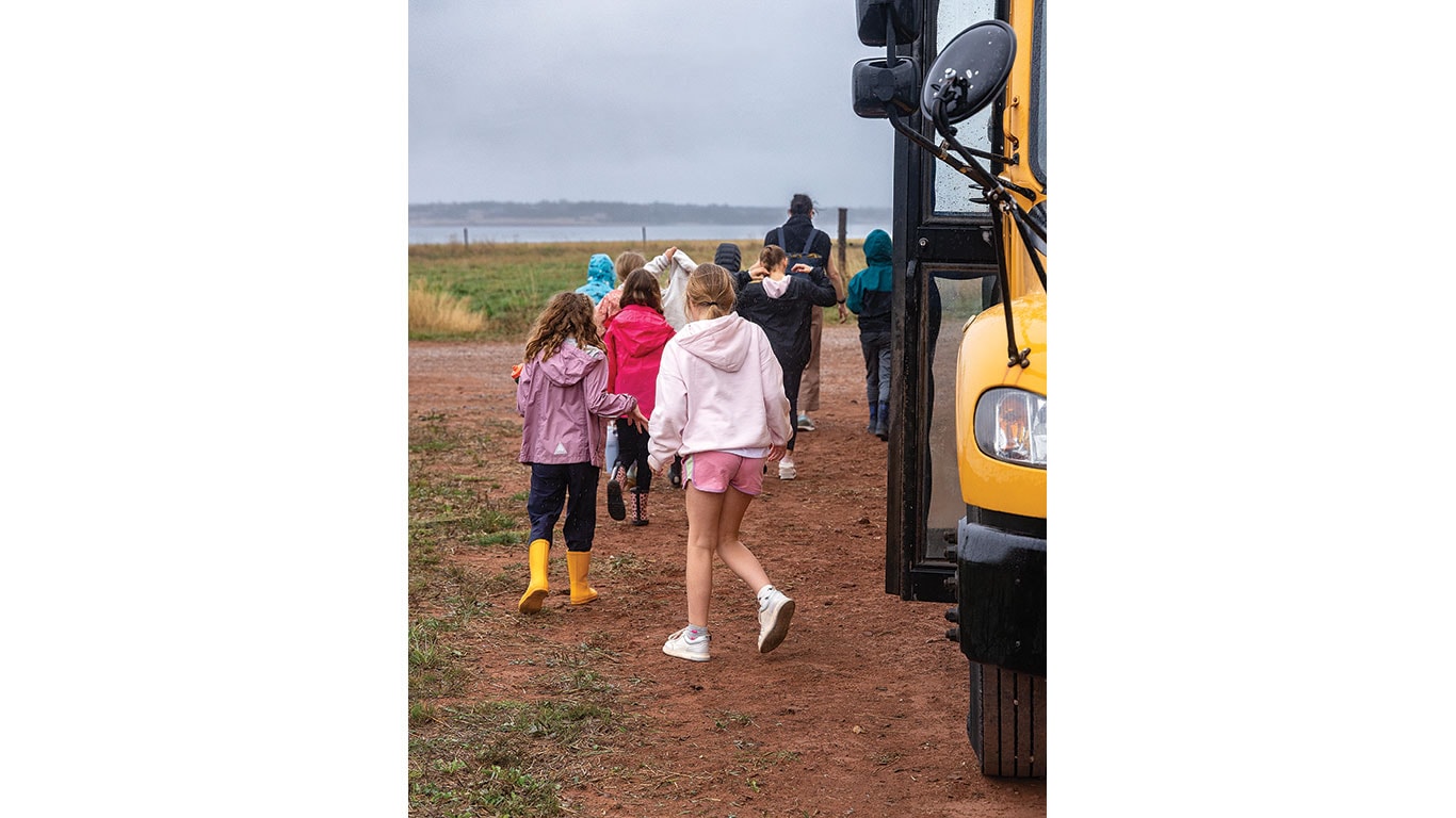 Children walk away from a school bus toward a farm field.