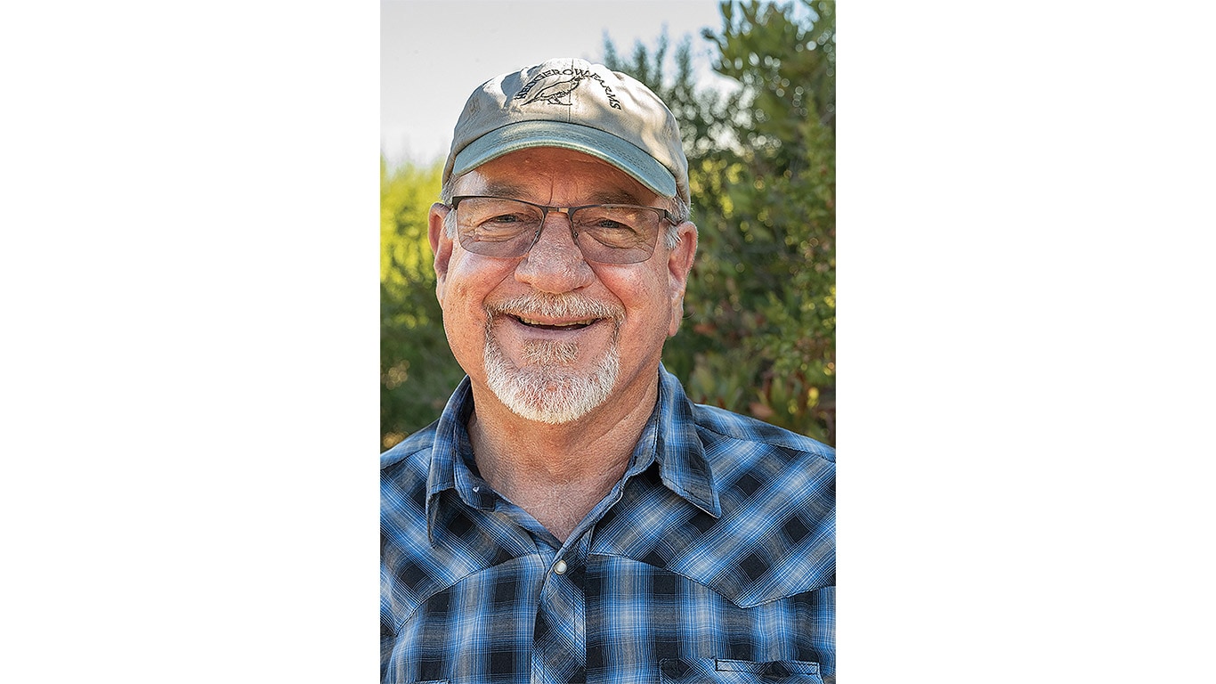 Person wearing glasses and a cap outdoors, with trees visible in the background.