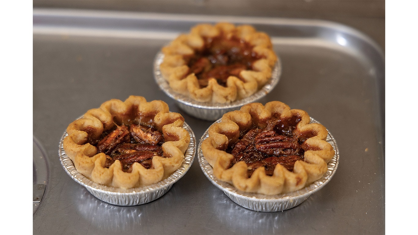 Three miniature pecan pies cooling on a stainless steel baking tray.