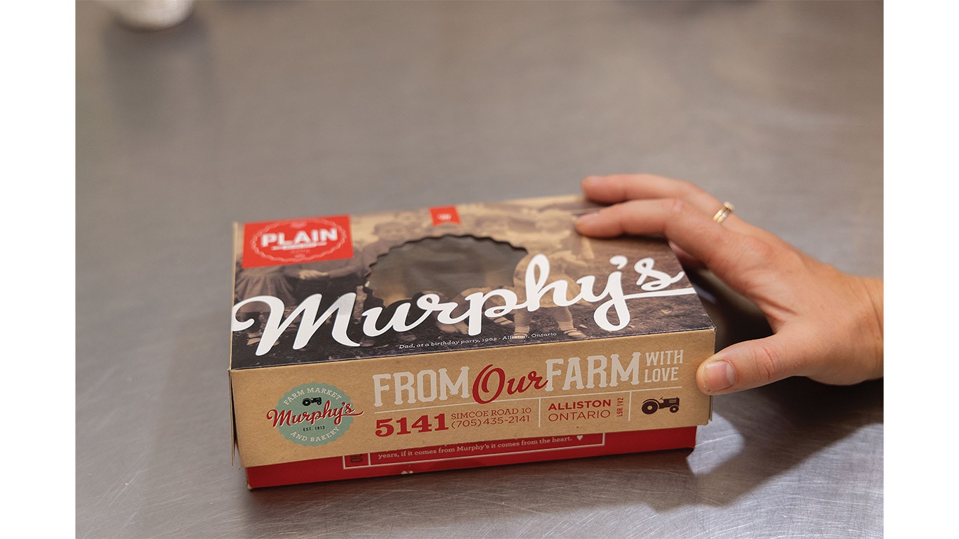 Hand placing a packaged baked pie product on a stainless steel work surface.
