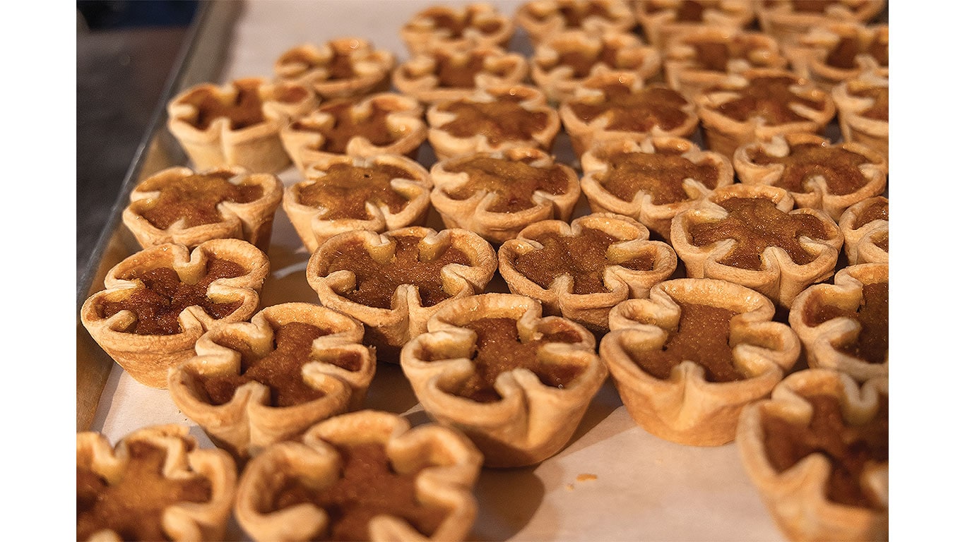 Rows of miniature baked pies arranged on trays in a commercial bakery setting.