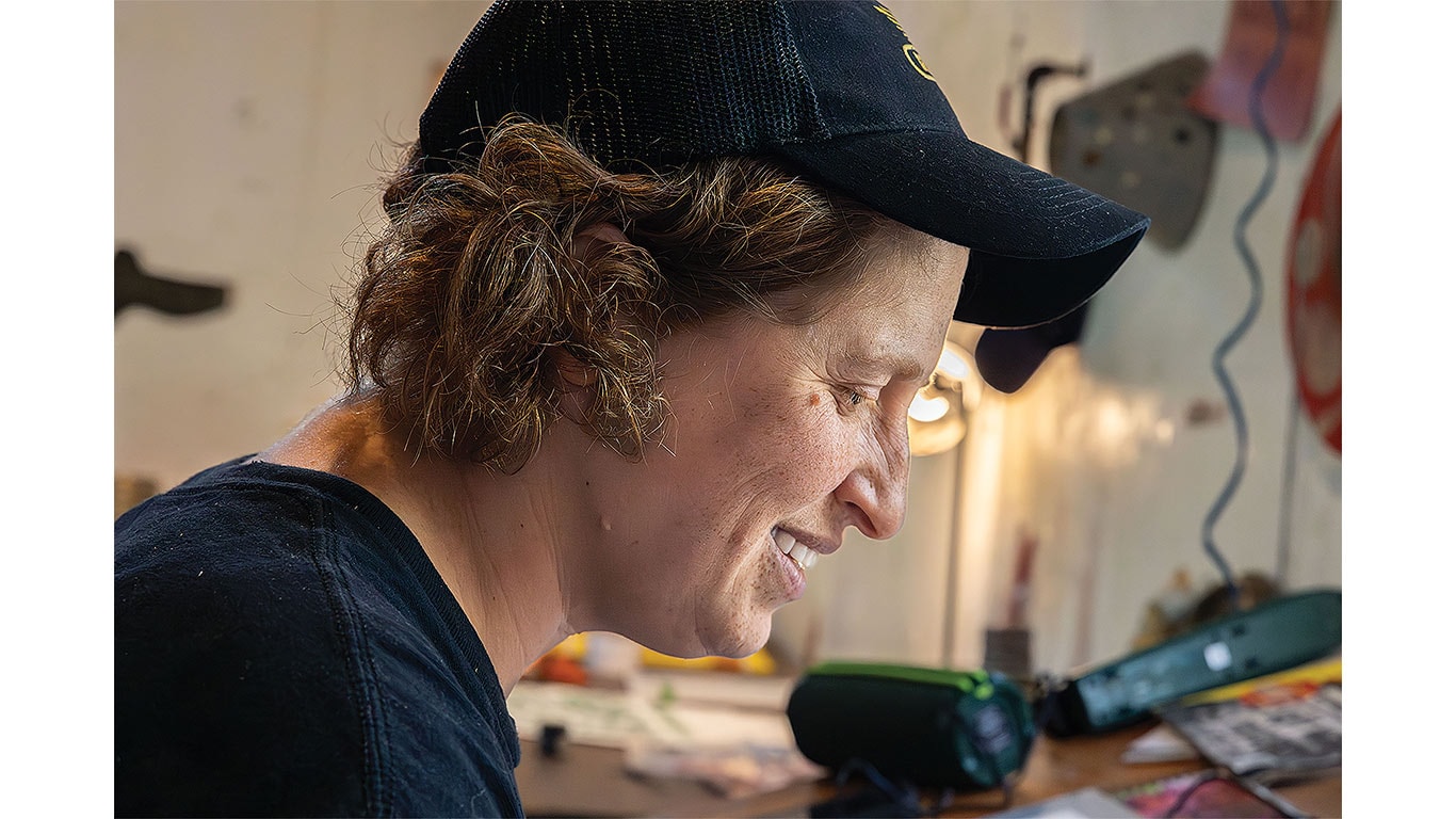 Person wearing a black cap works at a bench with tools and equipment in a workshop.