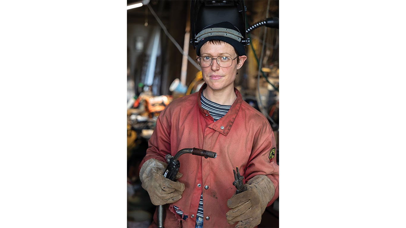 Person in protective welding gear holds welding equipment in a workshop.