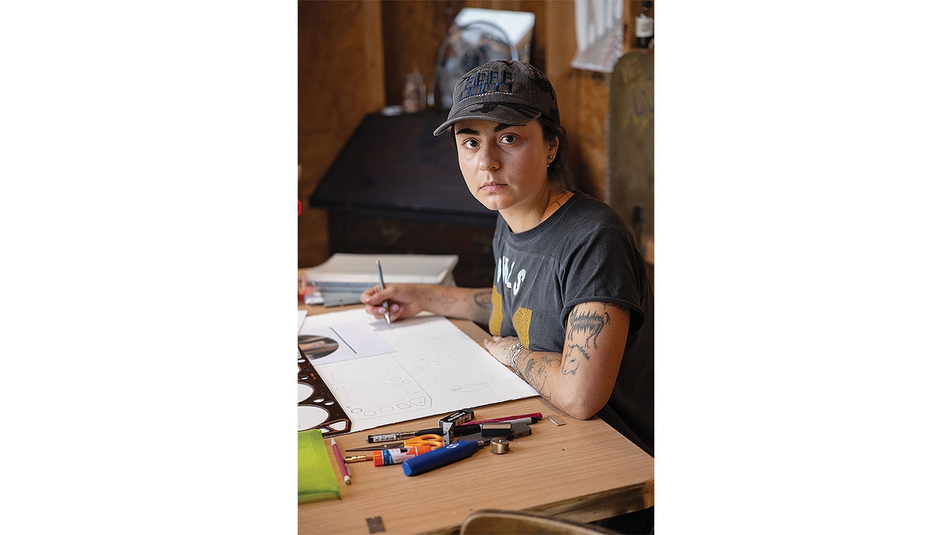 Person sketching designs at a worktable with drawing tools and materials nearby.
