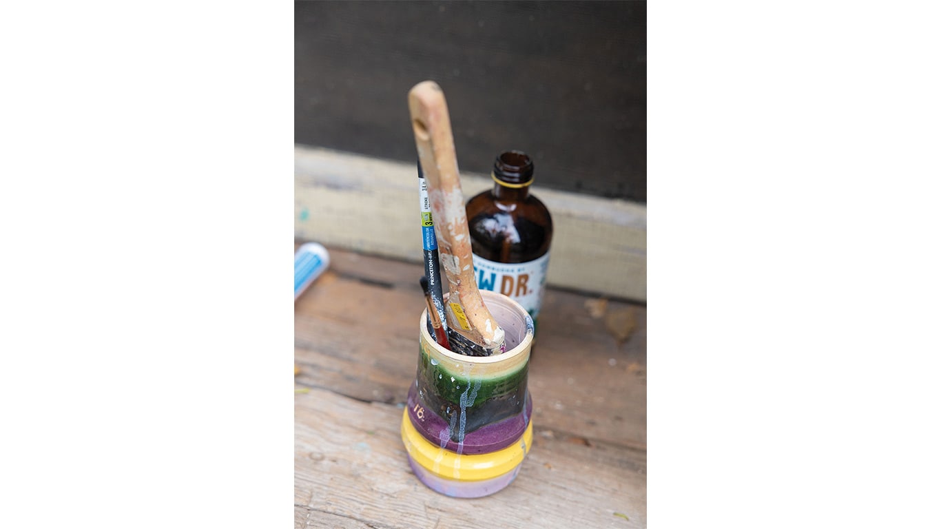 Paintbrushes and tools in a ceramic container on a wooden workbench.