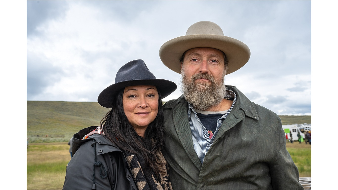 Two people wearing wide-brimmed hats standing outdoors in a grassy landscape.
