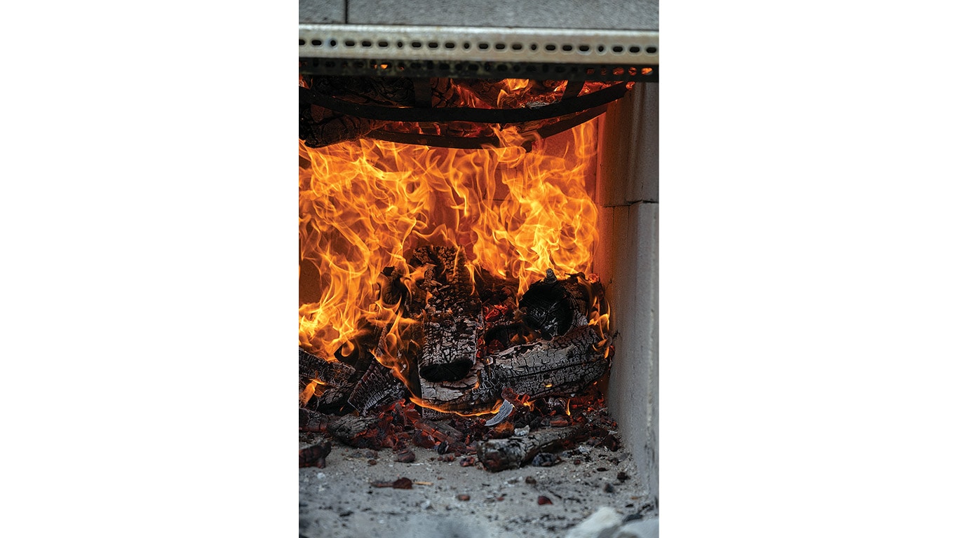 Flames and glowing embers burn inside a wood-fired cooking pit.
