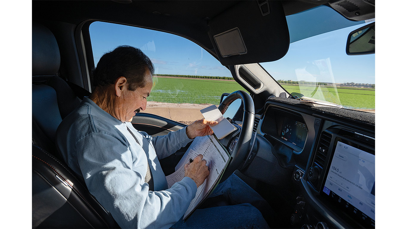 Person recording crop data on a clipboard while parked beside a cultivated field.