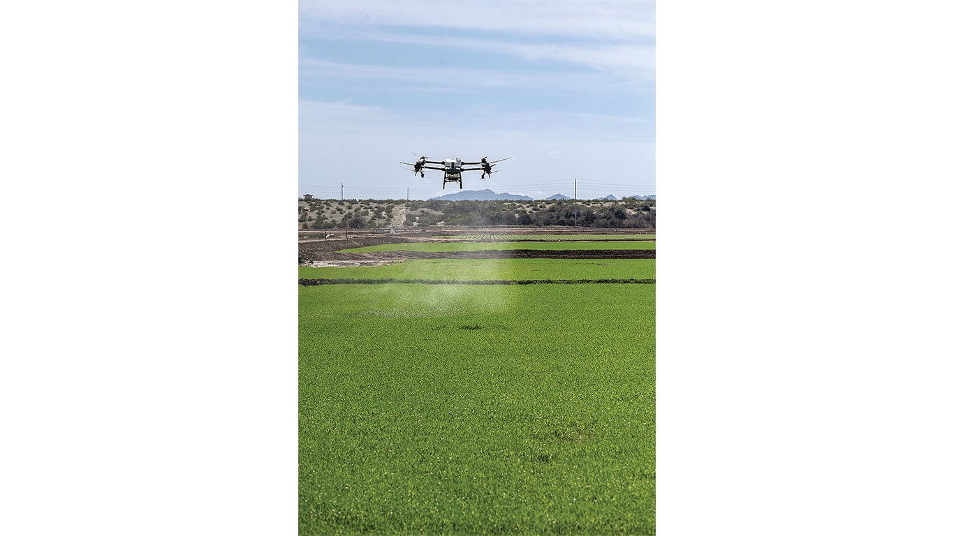 Agricultural drone spraying crop treatment over a green field during daylight.