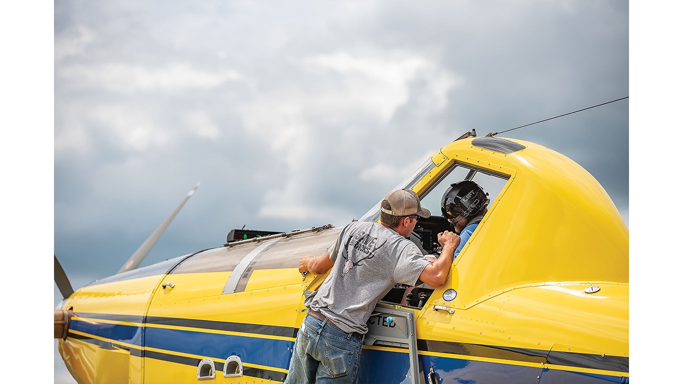 Ground crew member speaks with a pilot in the cockpit of a crop-dusting aircraft.