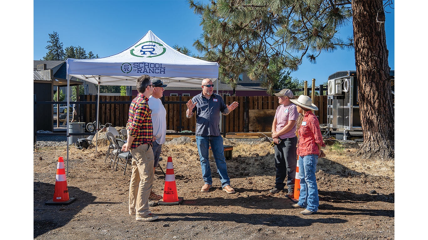 Group of people gathered outdoors near a canopy tent during a ranch education event.