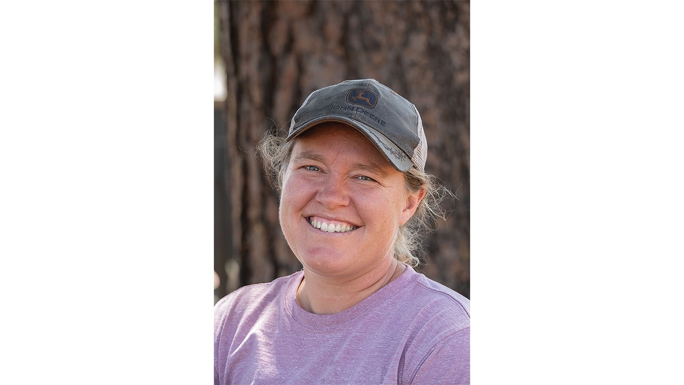 Person wearing a cap outdoors in front of a tree trunk.