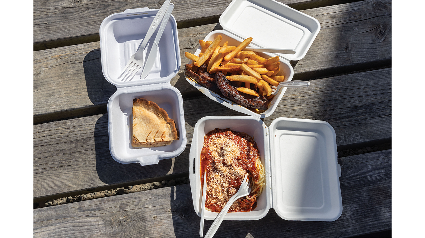 Containers full of spaghetti, boar meat, fries, and pie on a wooden table.