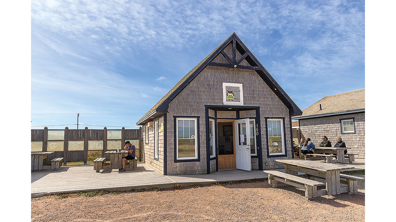 Small coastal restaurant with outdoor picnic tables under a bright blue sky.