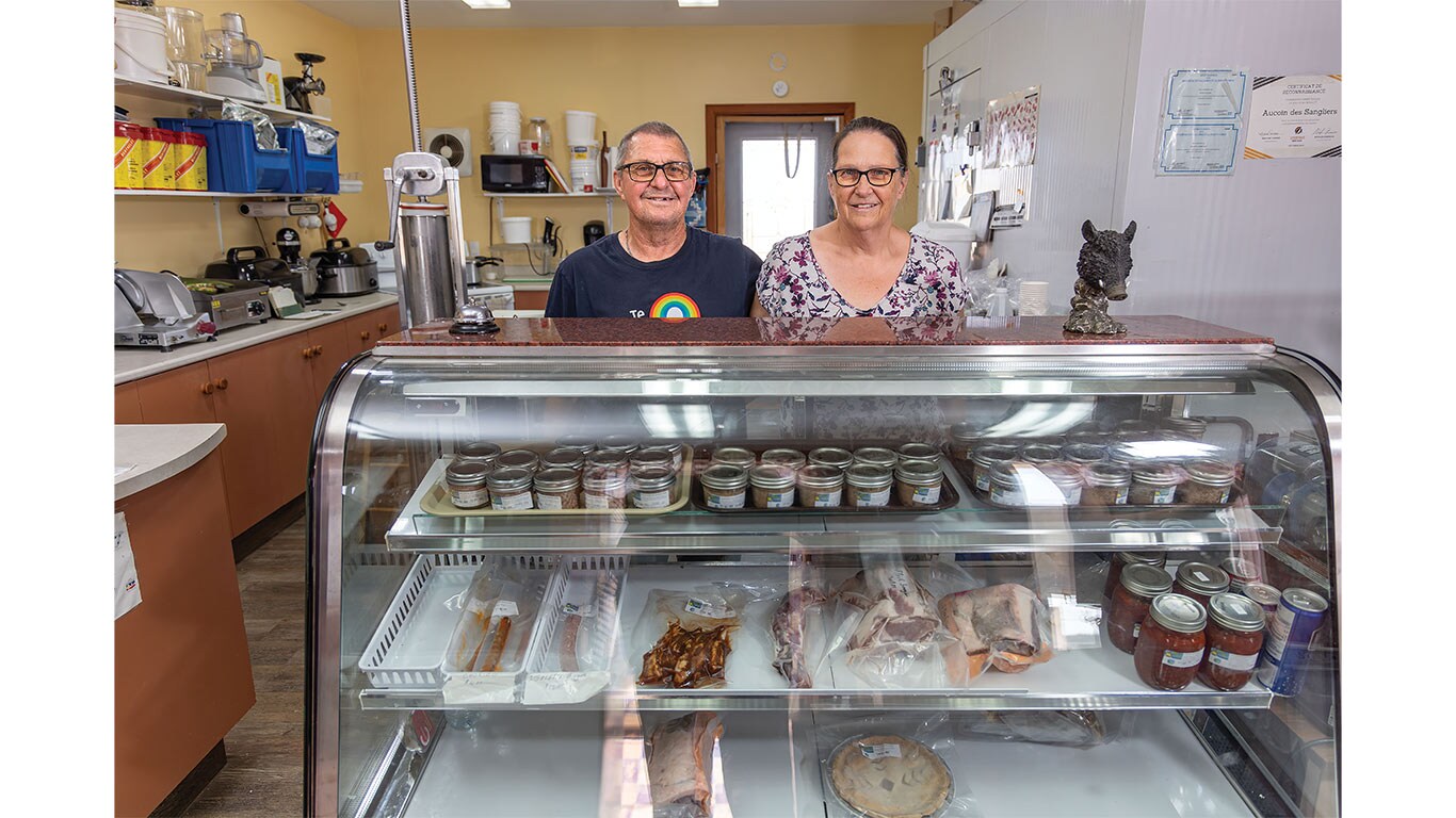 Two shop owners stand behind a display case of locally prepared foods and preserves.