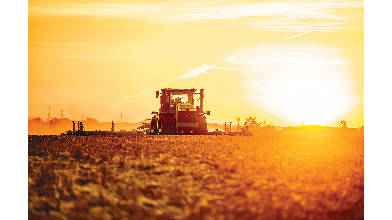 Tractor in a field pulling tillage equipment during sunset.