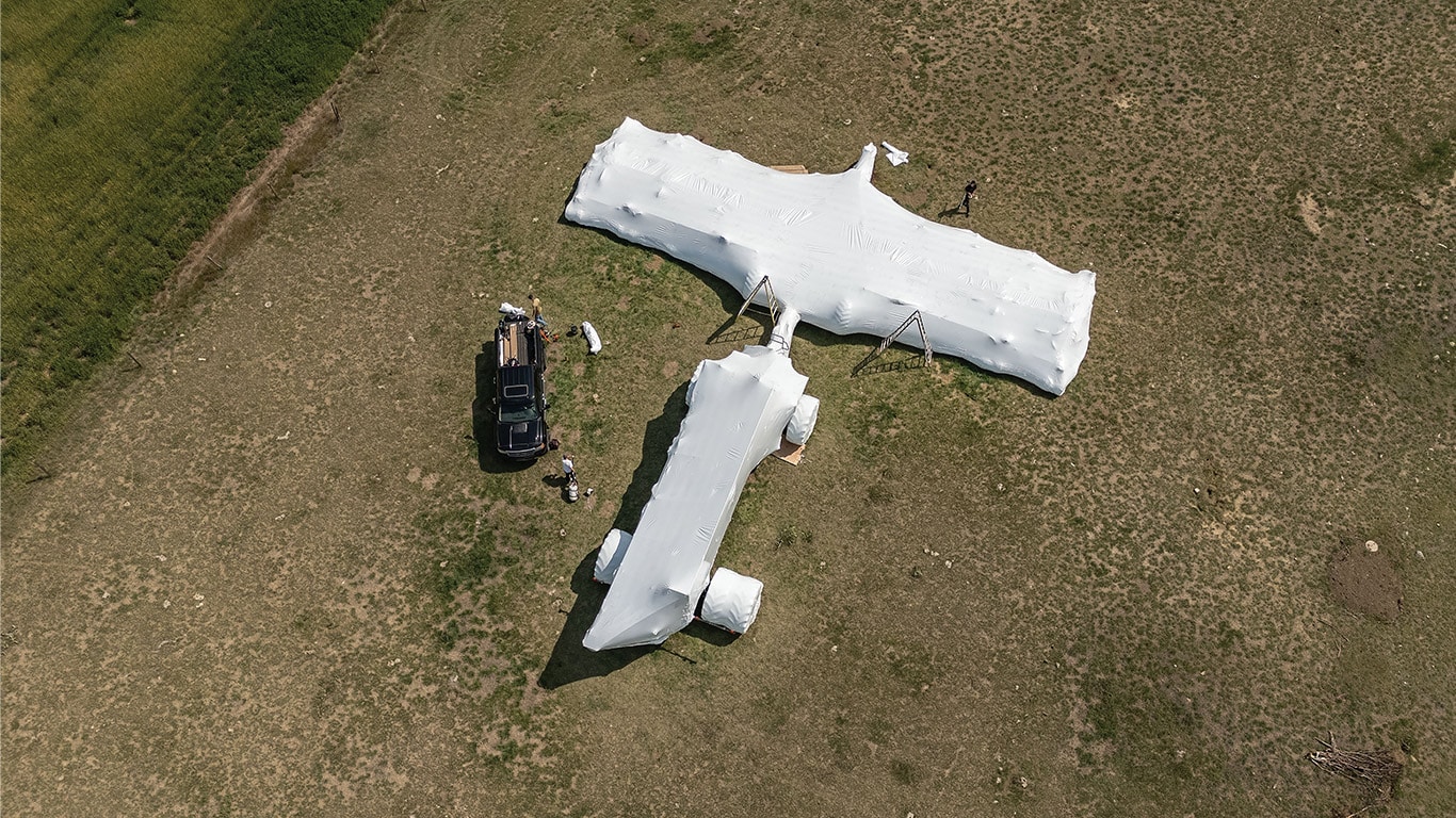 A large tarp covering farm machinery in an empty field.