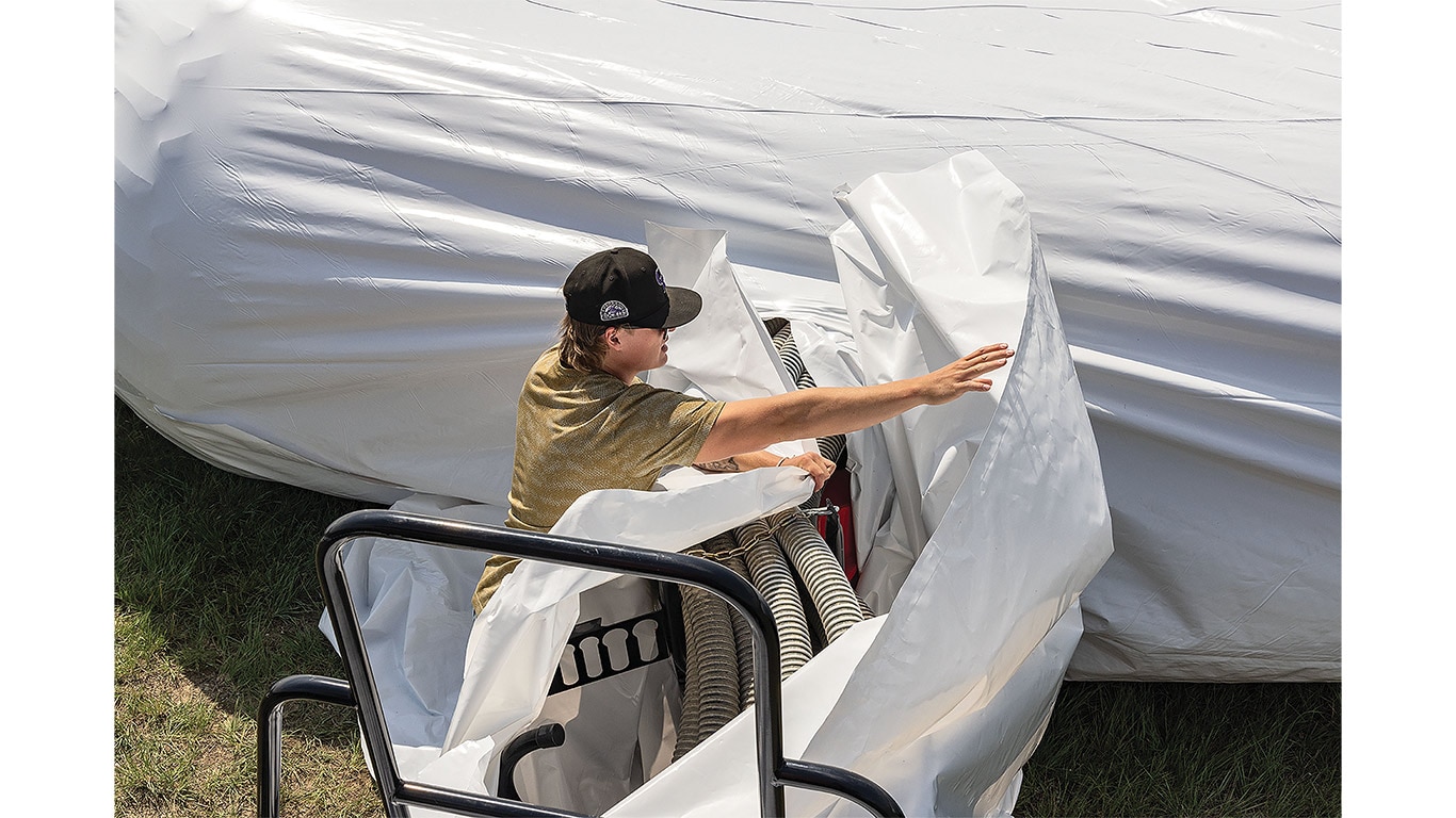Person adjusting plastic sheeting around farming equipment outside on a sunny day.
