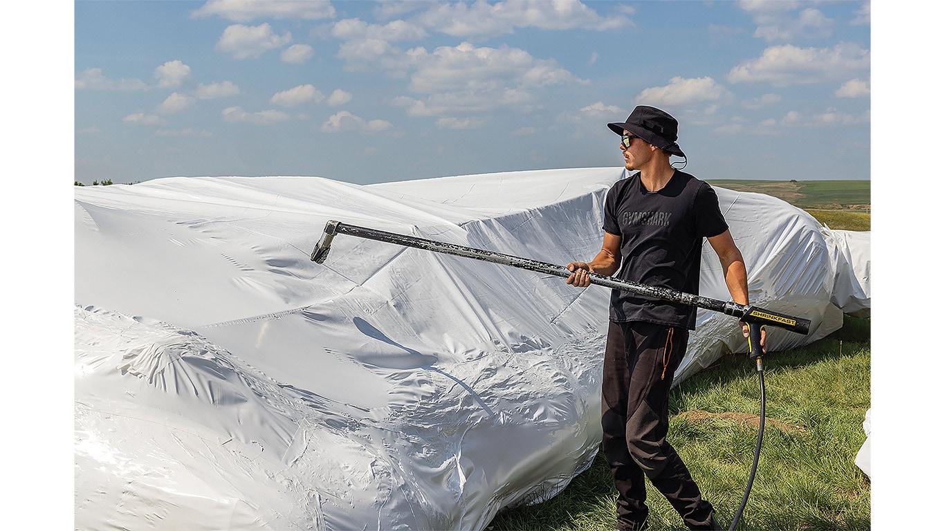 Person sealing plastic-covered farm equipment with a heat tool in a farm field.