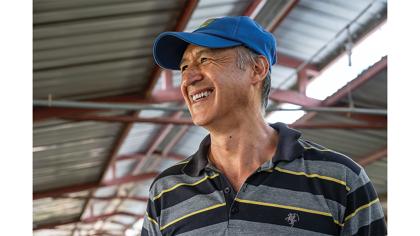 Person wearing a blue cap standing inside a farm building with metal roof supports.