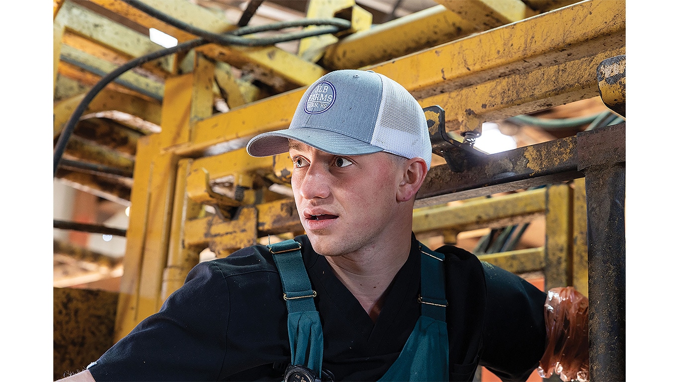 Individual with baseball cap and wearing overalls standing in front of equipment