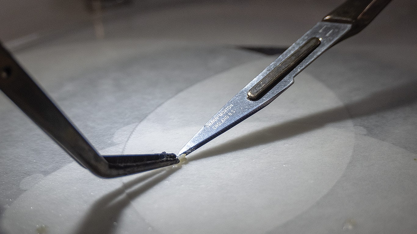 Two precision tools holding a tiny sample under bright light.