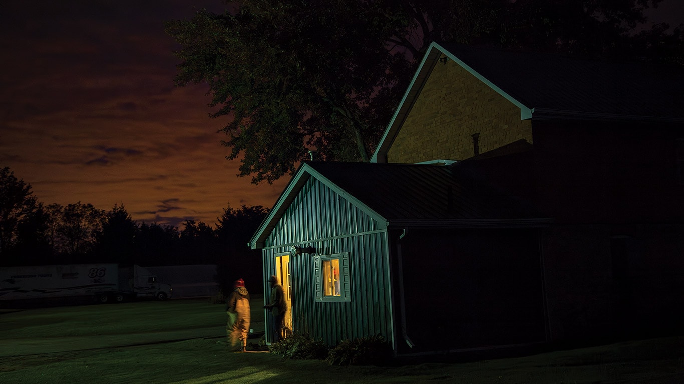 Person entering a small lit building at night with dark sky and trees in background.