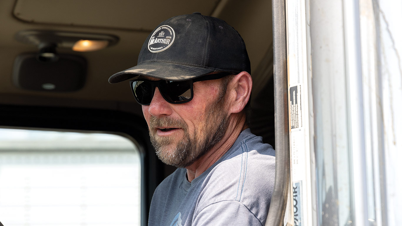 Person wearing a cap and gray shirt sitting inside a vehicle near an open door.